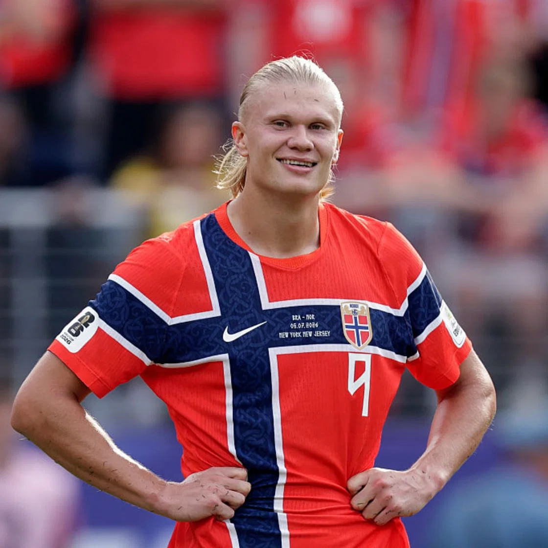 Erling Haaland in a Norway shirt, hands on hips, smiling